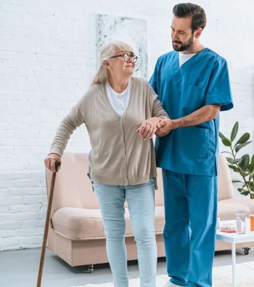 male nurse supporting senior woman in eyeglasses with walking stick